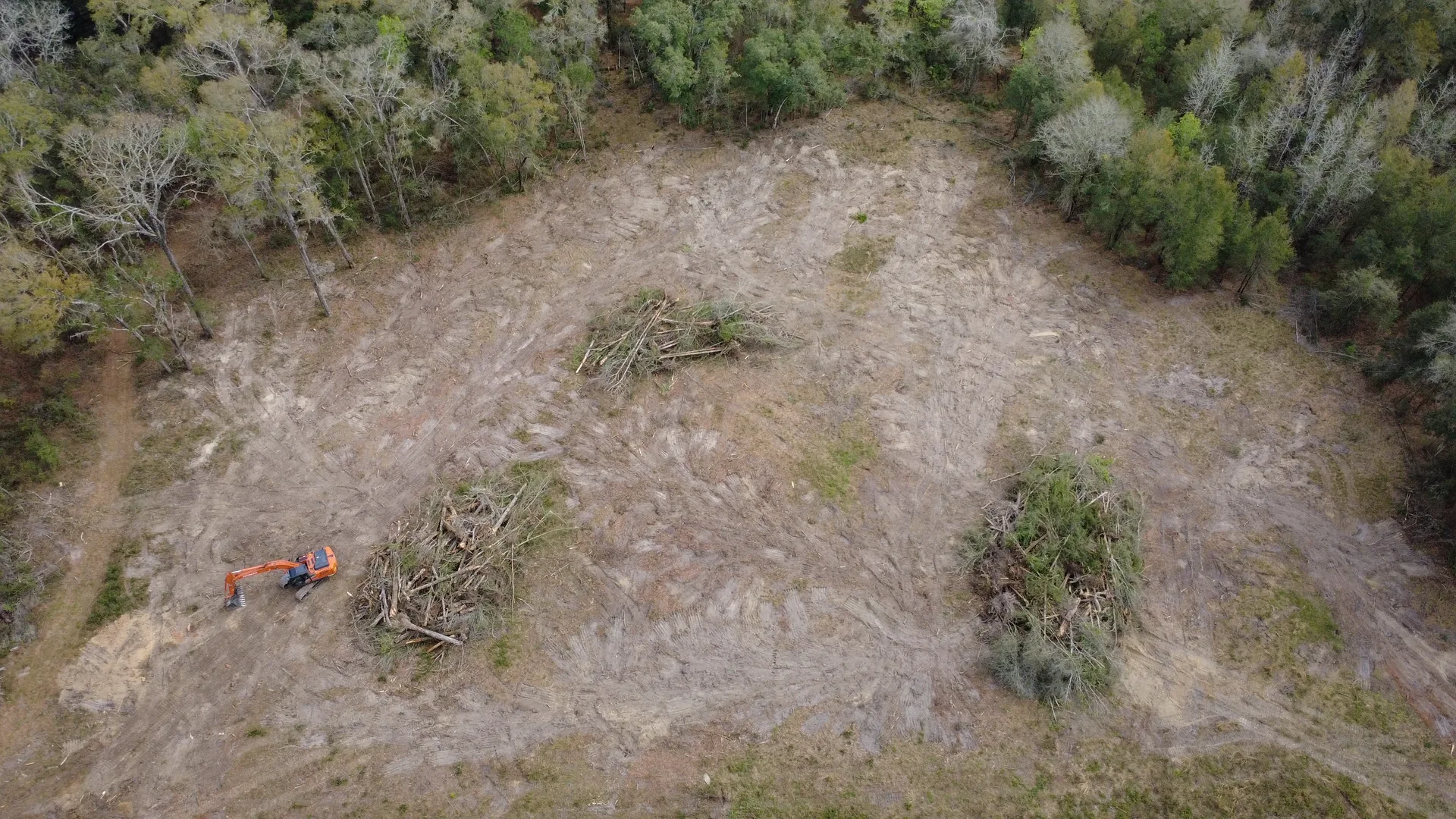 Aerial drone photo of a land clearing job in progress near Starke, Florida, excavator working between brush piles